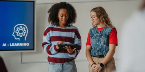 Two women are looking at a tablet, with a screen shows 