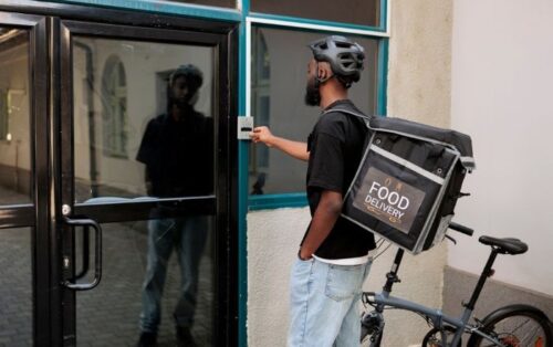Black food delivery man on bike rings doorbell