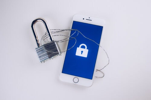 A small silver lock intwined with a wire and next to a phone.