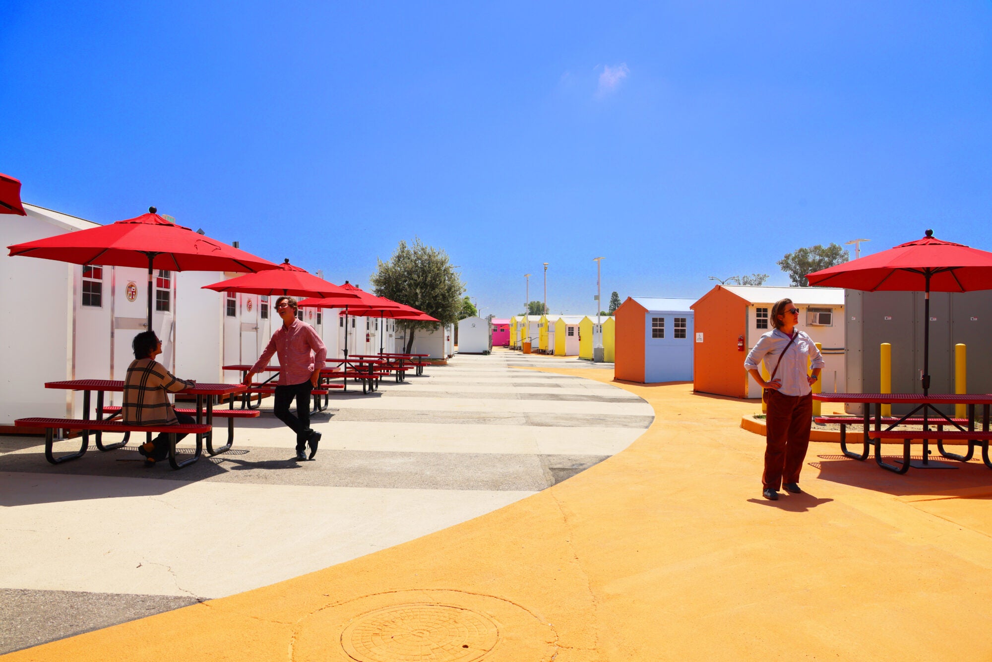 Courtyard with tables and red umbrellas on the left, surrounded by pre-fabricated tiny homes painted in bright orange, blue and yellow.