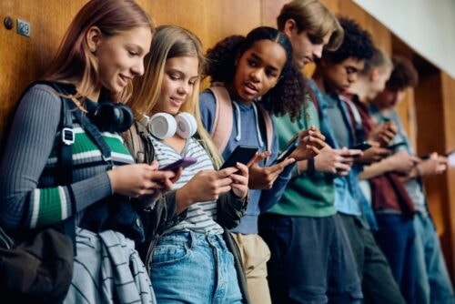 High school students lean against a wall, all using their smartphones.