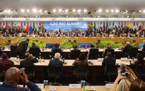 Wide view of delegates at the G20 Rio Summit, with national flags behind them and photographers in the foreground.
