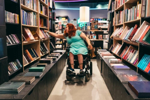 Woman in green dress sitting in wheel chair selecting a book