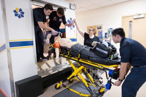 Four students practicing loading a dummy into an ambulance