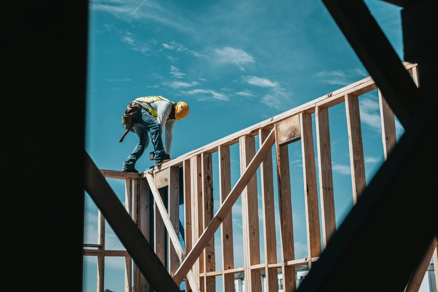 Construction worker standing on top of a wall frame of a building under construction, with blue sky in the background.
