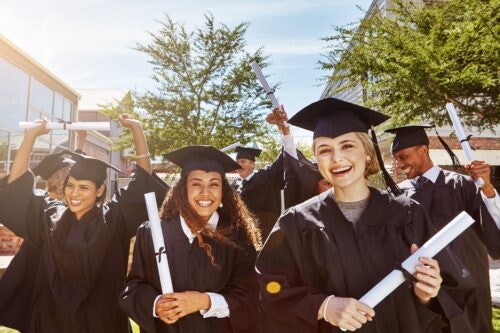 Happy college graduates wearing robes and graduation hats hold their diplomas.