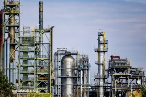 Industrial processing plant with metal towers, tanks, pipes, and scaffolding beneath a blue sky.