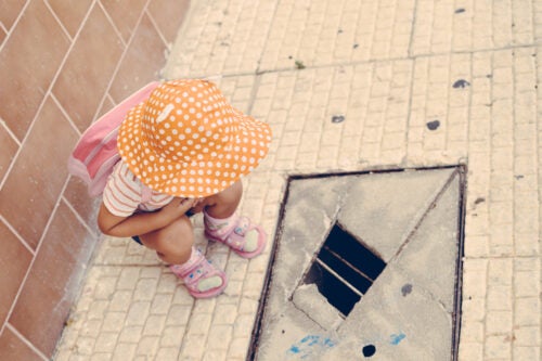 A child wearing a big hat stares at a hole in the sidewalk