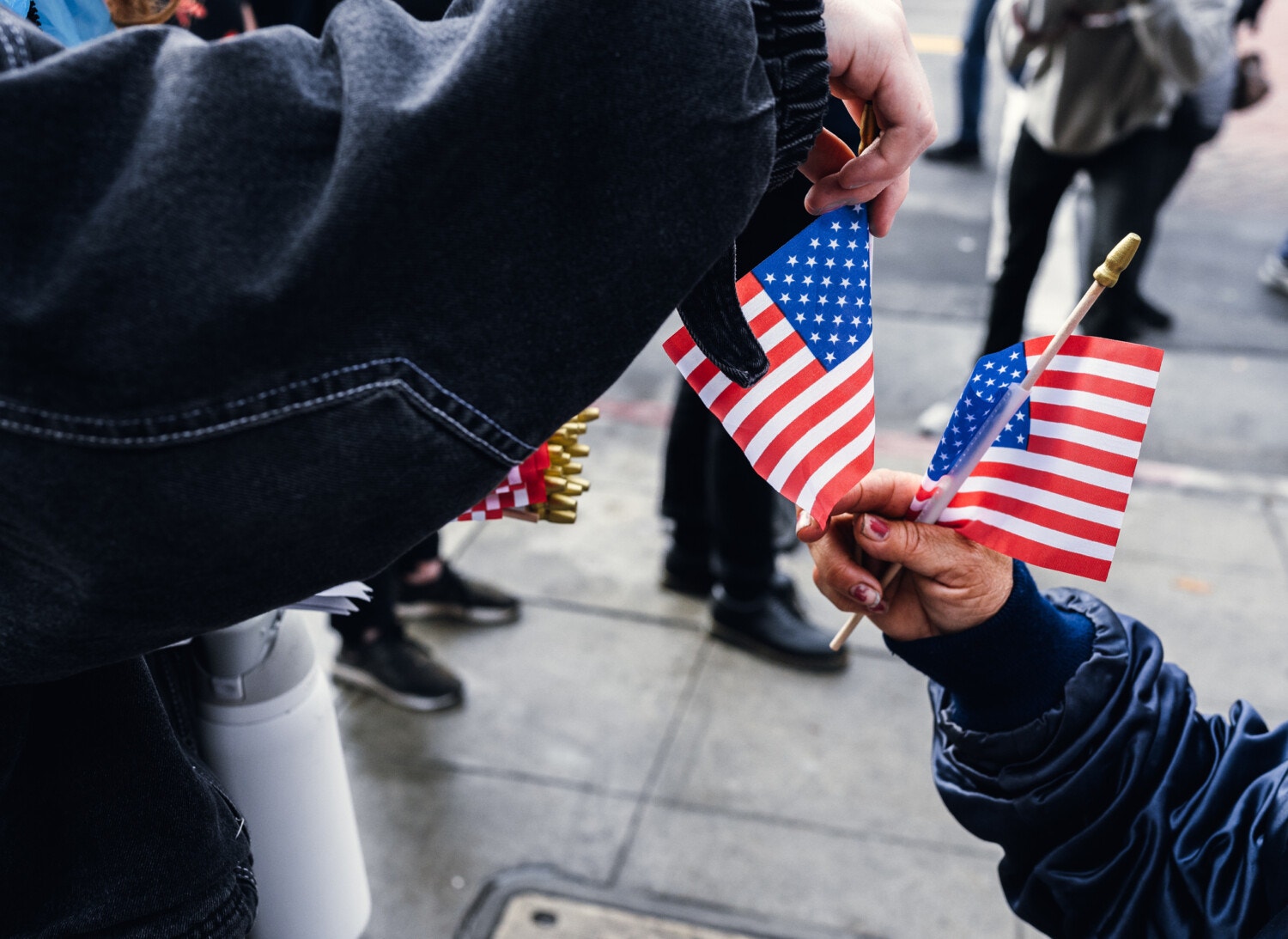 One person hands miniature American flags to another, with only their arms visible.