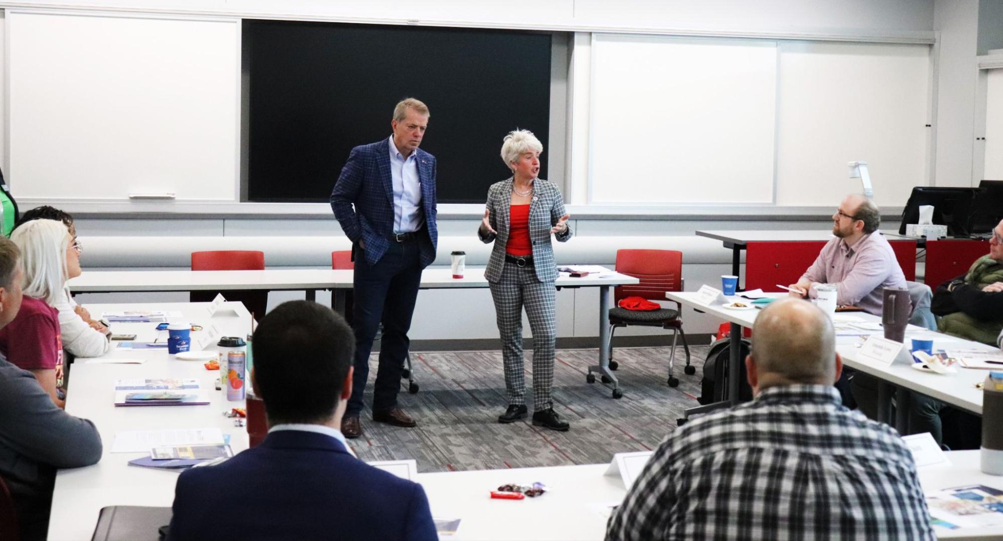 Two people speaking in a classroom while others listen.