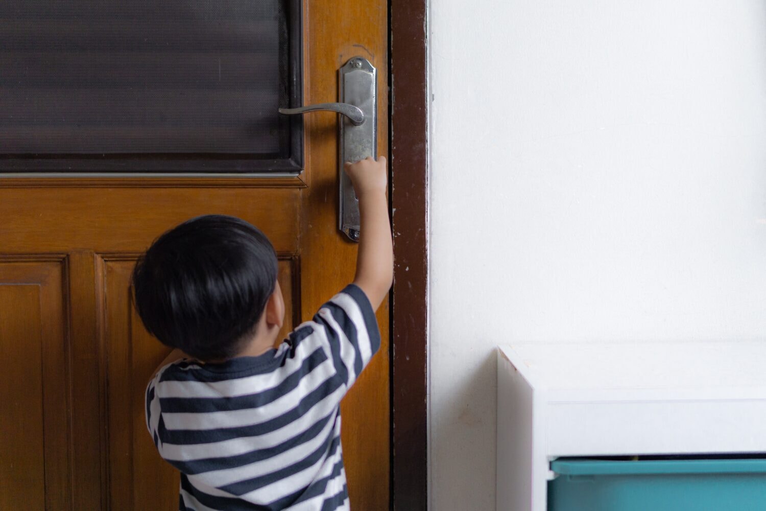 Child in a striped shirt reaches for the handle of a wooden door