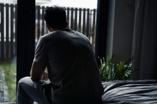 Dark image of a person sitting on a bed looking out through the window