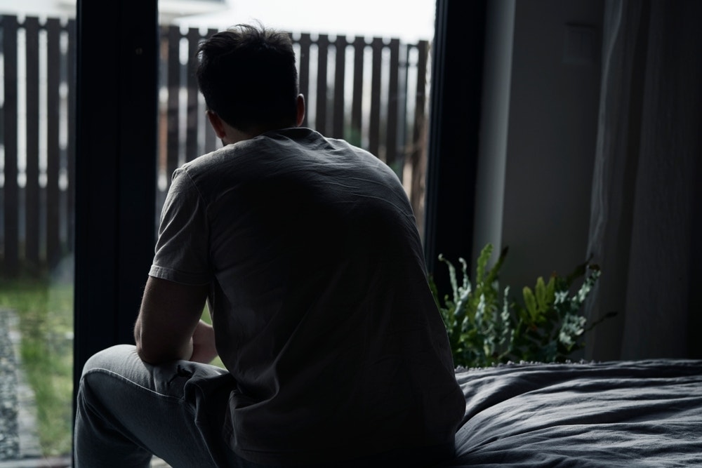 Dark image of a person sitting on a bed looking out through the window