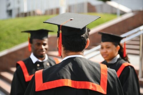 Three graduates in caps and gowns talking to each other